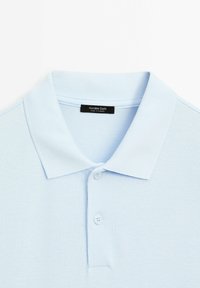 Polo bleu clair avec col côtelé et deux boutons, avec une étiquette noire indiquant "Massimo Dutti Made in Turkey."