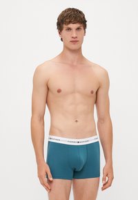 Teal színű boxer alsó, pamut keverékből készült, fehér elasztikus derékkal, amelyen logó található. Sima textúra, testhezálló fazon és közepes magasságú kivágás.