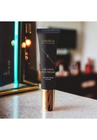 Krem pod oczy 24K Gold w czarnej tubce ze złotym napisem i złotą podstawą, umieszczony na marmurowej powierzchni z delikatnym, rozmytym tłem oświetleniowym.
