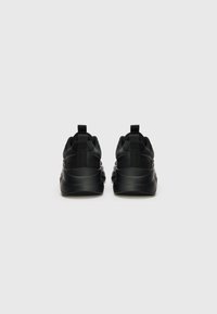 Black athletic sneakers featuring a smooth fabric upper, textured detailing, and a padded collar. Flat rubber sole and pull tab at the heel.