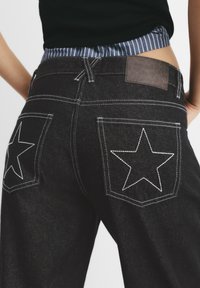Jeans in denim nero con tasche posteriori a stella, cuciture bianche a contrasto e un'etichetta in pelle beige sulla vita.
