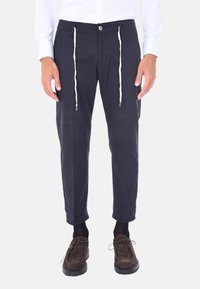 Pantaloni navy in cotone con vestibilità ampia, dotati di vita con cordino, orli cuffi e chiusura a bottone. Abbinati a scarpe marroni.