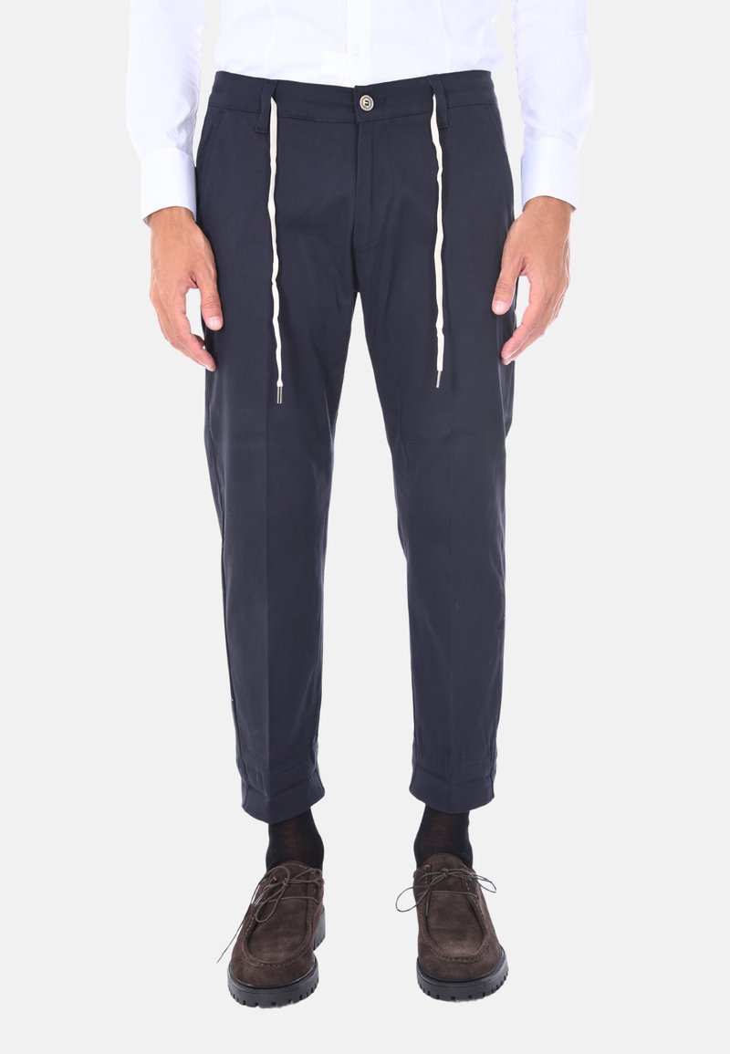 Pantaloni navy in cotone con vestibilità ampia, dotati di vita con cordino, orli cuffi e chiusura a bottone. Abbinati a scarpe marroni.