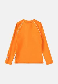 Camisa de manga larga de tejido naranja brillante. Presenta mangas raglán y un cuello redondo. Incluye costuras blancas y un acento de logo en la manga.