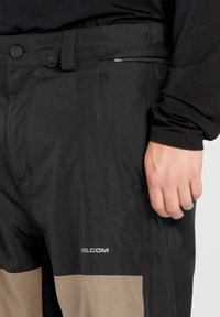 Zwarte en tan Volcom-broeken hebben een strak ontwerp met een knoopsluiting, een geavanceerde ritszak en een gladde, waterafstotende stof.