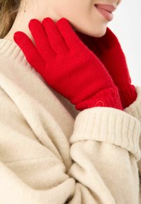 Gants tricotés rouges avec des poignets côtelés, fabriqués en un matériau doux, portés contre un pull crème. Gros plan montrant la texture et les détails.