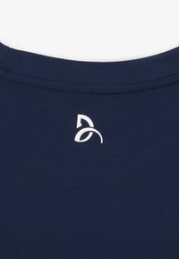 Encolure en tissu bleu foncé avec un petit logo abstrait blanc centré sous la couture du col.