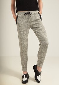 Grå strikkede joggingbukser med sorte sidelommer, elastisk talje og snøre. Blød tekstur, tapered ben design. Parret med sorte og hvide sko.