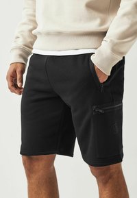 Shorts noirs en tissu doux, dotés d'une poche latérale zippée et d'un design élégant, idéaux pour une tenue décontractée.