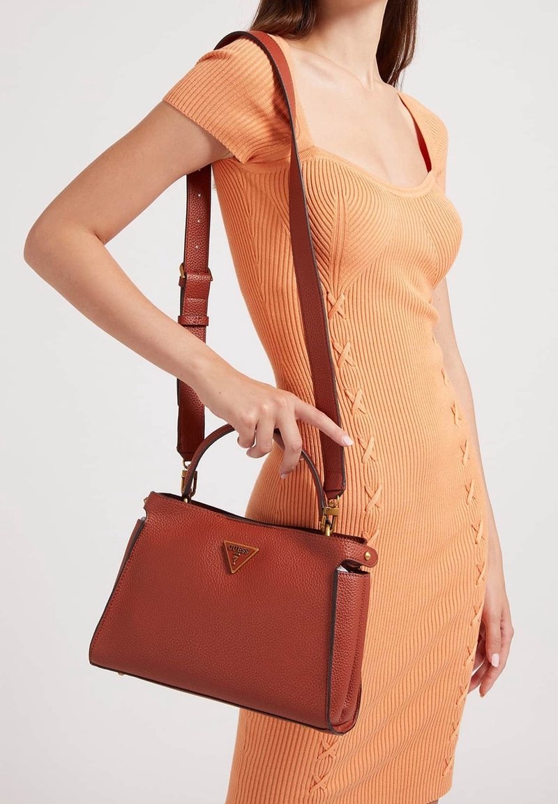 Femme portant une robe en maille orange à manches courtes tenant un sac à main en cuir marron avec poignée supérieure et bandoulière.