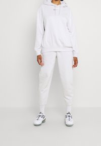 Ljusgrå hoodie med dragsko, avslappnad passform och ficka. Matchas med tapered sweatpants. Skor: klumpiga vita sneakers.