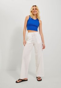 Cropped blue ribbed tank top, white wide-leg linen pants with drawstring, black flip-flops, minimal accessories, neutral background.