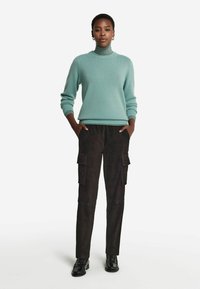 Jasnoniebieski wełniany sweter z golfem, z prążkowanymi mankietami i dołem, w połączeniu z czarnymi zamszowymi spodniami cargo z kieszeniami po bokach i luźnym krojem.