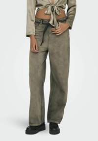 Lanneleveit i falmet olivengrønn denim, med en snor i livet og en avslappet passform. Kombinert med en kort satin topp og svarte sko.