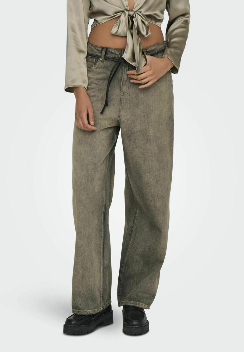 Lanneleveit i falmet olivengrønn denim, med en snor i livet og en avslappet passform. Kombinert med en kort satin topp og svarte sko.