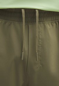 Olivgröna träningsshorts med elastisk midja, utrustade med snoddar och ett mjukt, strukturerat tyg. Inga synliga fickor.