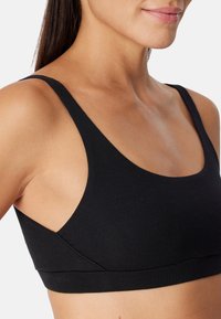 Svart ribbad bralette med tunna axelband, rundad halslinning och sömlös design. Tyget har en mjuk textur och en åtsittande passform.