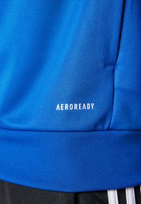 Blå atletisk stoff med en teksturert overflate; har en hvit "AEROREADY" logo på den nedre delen; inkluderer en svart elastisk midjebånd.