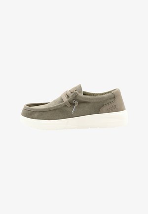 Mocassin décontracté en toile verte olive avec lacets beige, col rembourré et semelle épaisse en caoutchouc blanc, présenté de profil sur fond blanc.