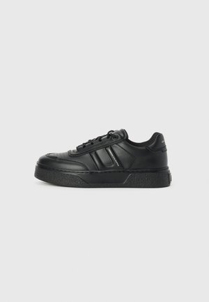 Zwarte platform sneakers van glad leer, met een laag profiel, ronde neus, getextureerde zool en drie zijsstrips voor een designdetail.