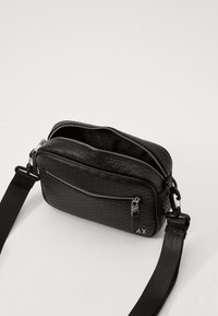 Borsa a tracolla nera in ecopelle testurizzata, con due scomparti con zip, tracolla regolabile e logo sul lato.
