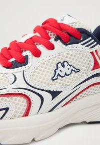 Hvite treningssko med røde snører og marineblå detaljer, med mesh-design, gummisåle og en logo på siden.