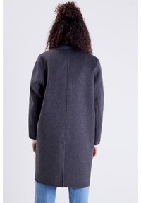 Abrigo de lana gris con mangas largas, silueta recta y costura central. Presenta un cuello alto y llega hasta medio muslo.