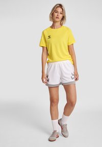 Gul lättvikts sportt-shirt med korta ärmar och logotyp, kombinerad med vita shorts med grå accenter och zickzack-mönster.