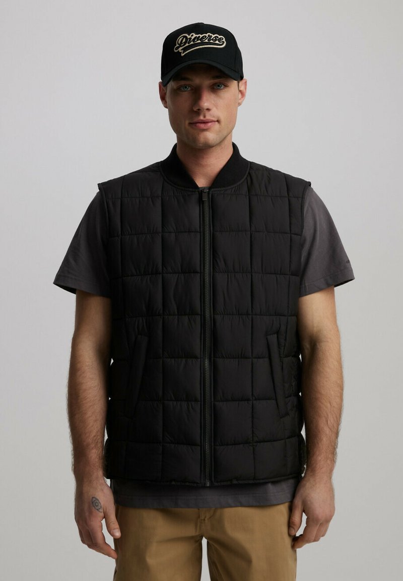 Czarna pikowana kamizelka z wysokim kołnierzem i zamkiem błyskawicznym z przodu. Posiada dwie boczne kieszenie. Nosi się ją na szarej koszulce, w zestawieniu z khaki spodniami.