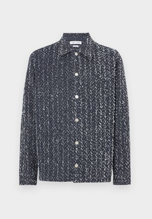 Granatowa koszula na guziki z teksturowanej, wzorzystej tkaniny z białymi akcentami. Kołnierzyk, długie rękawy, luźny krój. Widoczne srebrne guziki.