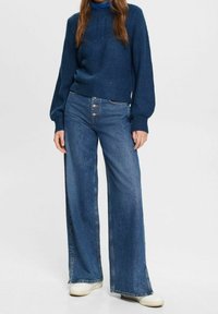 Blauer, gerippter Pullover mit langen Ärmeln und Rundhalsausschnitt, kombiniert mit weit geschnittenen blauen Denim-Jeans mit Knopfverschluss und dezenter Waschung.