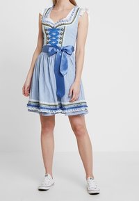 Robe dirndl bleu clair avec un corsage ajusté, un devant lacé, des manches à volants et un nœud en satin à la taille. Ourlet et bordure brodés.