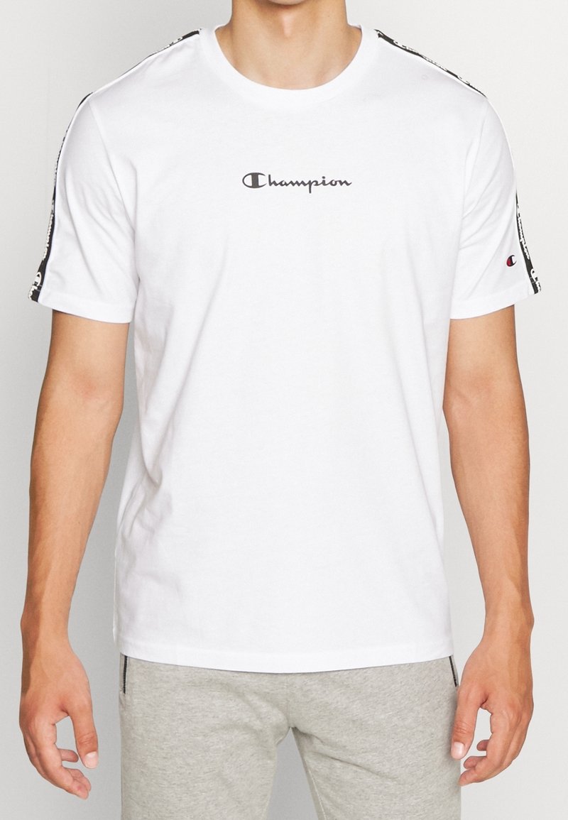 Hvid bomulds T-shirt med korte ærmer, prydet med et centralt "Champion" logo og sorte mønstrede detaljer langs skuldrene.