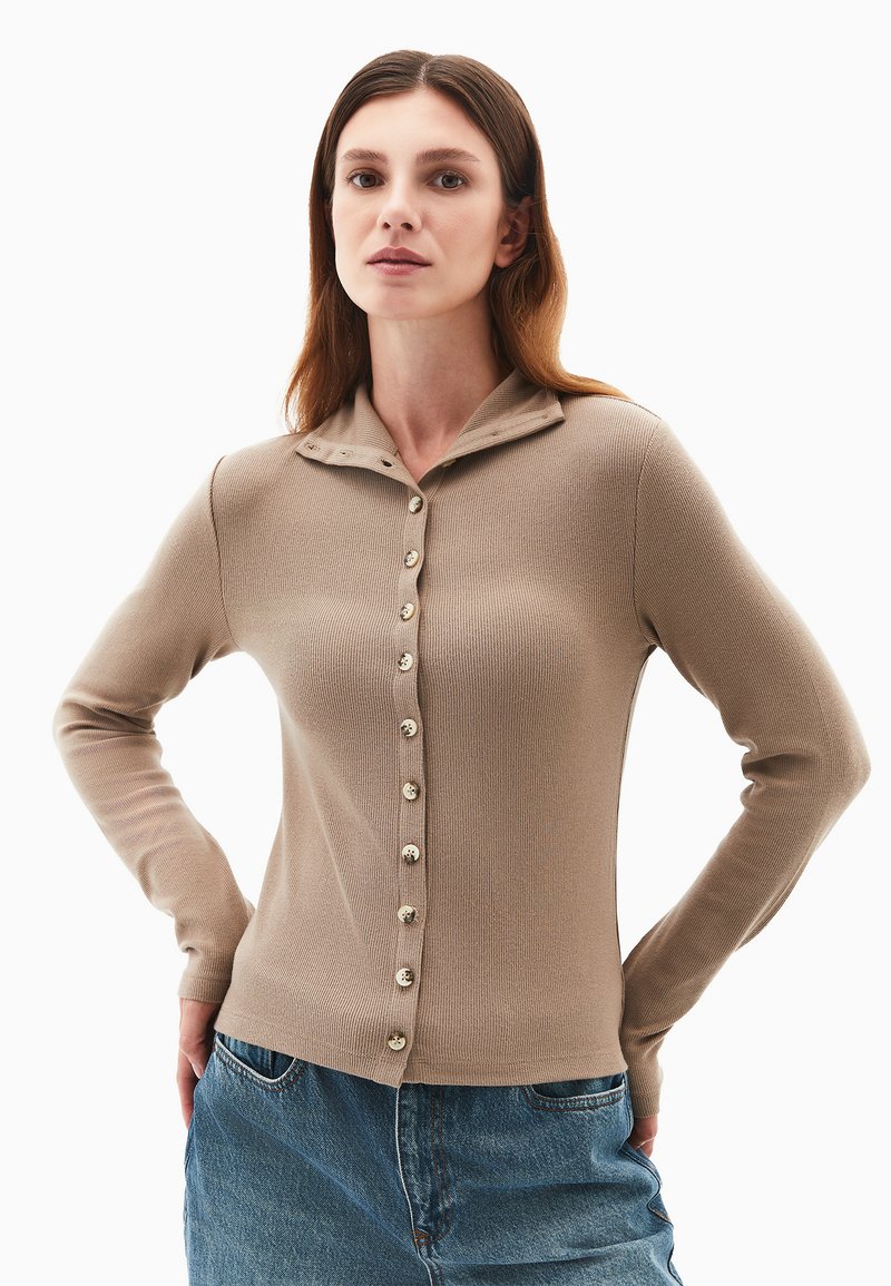 Beige ribbet sweater med krave, prydet med en række af seks runde knapper foran og lange ærmer. Teksturstrik materiale.