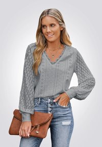 Gray blouse with lace detailing, scalloped neckline, long sleeves, and textured fabric, paired with distressed blue jeans and a brown clutch.