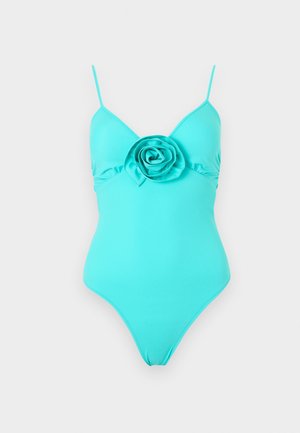 Turquoise one-piece swimsuit with thin shoulder straps and a large fabric rose detail centered on the chest.
