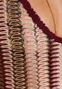 Top de crochet con franjas alternadas en burdeos, rosa y crema. La textura es abierta y calada, con líneas onduladas y un escote con borde en forma de concha.