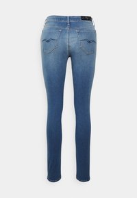 Vaqueros de mezclilla ajustados en un lavado azul medio, que cuentan con dos bolsillos traseros con un detalle de costura en zigzag y un desvanecimiento sutil a lo largo de las piernas.