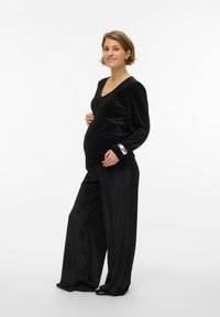 Melnas samta grūtniecības drēbes ar V-veida kakla izgriezumu, savilktām plecu daļām un platām biksēm. Augšdaļai ir dekoratīvi aproces detaļas.