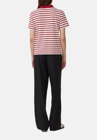 Rood-wit gestreepte katoenen t-shirt met een geribbelde kraag, gecombineerd met losse zwarte broek. Focus op eenvoud en comfort in het ontwerp.