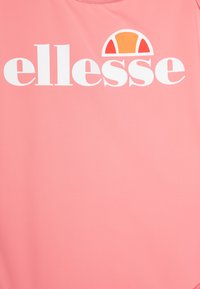 Roza majica iz gladkega materiala z drznim belim logotipom "ellesse" in večbarvno grafiko nad napisom.