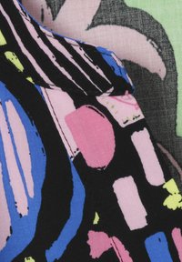 Farbiger Stoff mit kräftigen abstrakten Mustern, darunter Formen in Pink, Blau, Schwarz und Grün. Weiche Textur und sichtbare Nähdetails.
