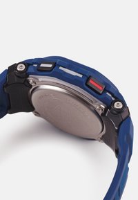 Blå armbandsur med en texturerad gummirem, med en baksida i rostfritt stål, svarta, röda och vita knappar på sidan, och en robust design.