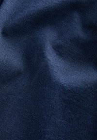 Tumši zila auduma virsma ar gludu tekstūru, kurā ir nedaudz izteiksmīgas krāsu un gaismas variācijas, kas liecina par austo materiālu. Nav redzamu rakstu vai detaļu.