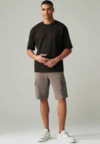 Brun t-shirt med kort ärm, grå cargo-byxor med sidofickor och vita sneakers. Slät textur, avslappnad passform, avslappnad design.