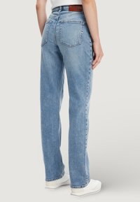 Jeans di denim azzurro chiaro a vita alta con vestibilità rilassata, caratterizzati da due tasche posteriori e un'etichetta in pelle marrone sulla cintura.