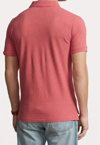 Rode poloshirt van een gestructureerde gebreide stof, met korte mouwen en een klassieke kraag. De zoom is iets gebogen en het is gecombineerd met blauwe jeans.