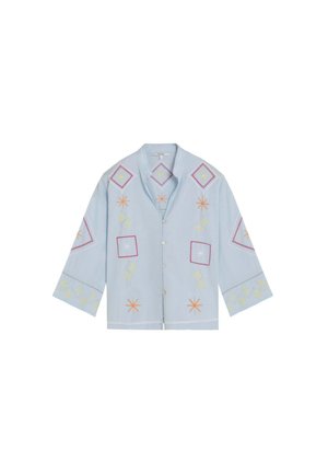 Camisa azul claro con botones y mangas anchas, con patrones bordados geométricos de estrella y cuadrado en naranja, amarillo y rojo.