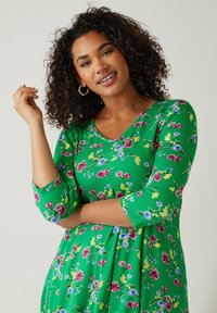 Grünes Blumenkleid mit Dreiviertelärmeln, ausgestattet mit einem runden Ausschnitt und einem lebendigen Druck von rosa, lila und gelben Blumen.