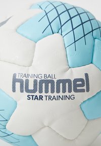 Hummel träningsboll har en vit och ljusblå färgskala med texturerade paneler och en randig logotyp. Rund form med en slät yta.